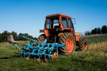 Trattore rosso con erpice blu in una fattoria. — Foto stock