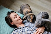Mujer acostada en el suelo rodeada por dos conejos de casa de mascotas - foto de stock