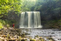 Cachoeira em cascata sobre um penhasco, em uma piscina de rocha, rio, pessoa em pé na margem do rio. — Fotografia de Stock