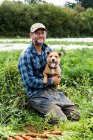 Farmer kneeling in a field, holding cute dog — Stock Photo