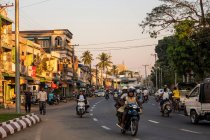 Mawlamyine, shop fronts and traffic on the road at sunset, motorbikes and pedestrians. — Stock Photo