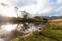 Мальчик играет на берегу реки, плоская спокойная вода и открытые пространства — стоковое фото
