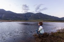 Un niño explorando la orilla de una laguna a la sombra de la cordillera Kleinriver - foto de stock
