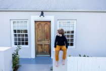 Giovane ragazzo seduto su un muro fuori dalla sua casa — Foto stock