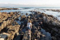 Niño trepando y explorando las rocas y las piscinas, De Kelders, Western Cape, Sudáfrica. - foto de stock