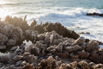 Dos niños explorando las rocas irregulares y las piscinas de rocas en la costa del Océano Atlántico, De Kelders, Cabo Occidental, Sudáfrica. - foto de stock