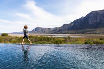 Rapaz de oito anos a caminhar à beira de uma piscina infinita, um cenário de montanha — Fotografia de Stock