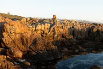Ragazza adolescente arrampicata sulle rocce sopra una piscina rocciosa sulla costa a De Kelders. — Foto stock