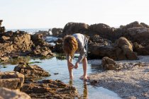 Jeune garçon explorant une piscine rocheuse parmi les roches dentelées de la côte de l'océan Atlantique au coucher du soleil, De Kelders, Cap-Occidental, Afrique du Sud. — Photo de stock