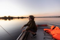 Um menino pescando de um barco nas águas calmas planas do Delta do Okavango ao pôr-do-sol, Botsuana. — Fotografia de Stock