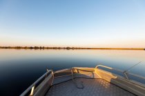 Um barco nas águas do Delta do Okavango ao pôr do sol, água calma plana e paisagem plana, Botsuana. — Fotografia de Stock