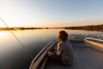 Young boy fishing at the stern of a boat in the Okavango Delta at sunset — Stock Photo