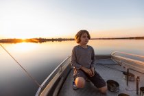 A young boy fishing from a boat on the flat calm waters of the Okavango Delta at sunset, Botswana. — Stock Photo