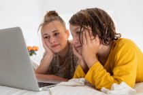 Мальчик и сестра-подросток делят ноутбук, смотрят в спальне — стоковое фото