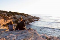 Adolescente et jeune frère au coucher du soleil, assis côte à côte regardant l'océan. — Photo de stock