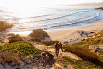 Jeune garçon et femme mûre grimpant un chemin de falaise au coucher du soleil. — Photo de stock