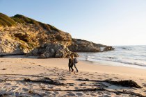 Duas pessoas caminhando ao longo de uma praia de areia, algas marinhas lavadas na costa — Fotografia de Stock