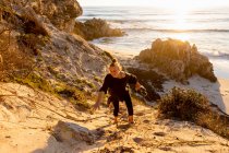 Teenage girl climbing up a very steep sandy slope above a beach — Stock Photo