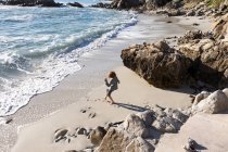 Маленький мальчик один на небольшом участке песка под скалами у океана. — стоковое фото