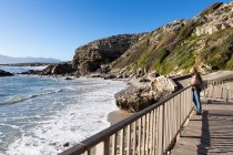 Uma mulher madura em pé em uma passarela com vista para uma praia de areia — Fotografia de Stock