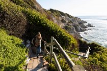 Donna adulta che sale i gradini fino alla cima di una scogliera sopra una spiaggia. — Foto stock