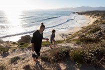 Un'adolescente e suo fratello corrono lungo un sentiero verso una spiaggia sabbiosa — Foto stock