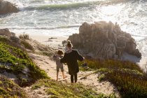 Una adolescente y su hermano corriendo por un camino hacia una playa de arena - foto de stock