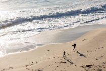 Dos niños corriendo y dejando huellas en la suave arena de una playa - foto de stock
