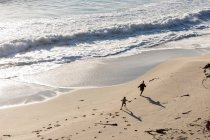 Dos niños corriendo y dejando huellas en la suave arena de una playa - foto de stock