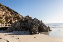 Due bambini appollaiati su rocce frastagliate che si affacciano su una spiaggia sabbiosa con bassa marea — Foto stock