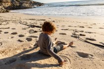Niño sentado en una playa de arena - foto de stock