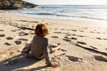 Jeune garçon assis sur une plage de sable — Photo de stock