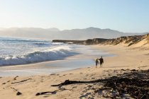 Dos personas caminando por una playa de arena, un adolescente y un niño - foto de stock