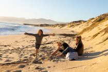 Сім'я, дочка і син сидять на піщаному пляжі з видом на море . — стокове фото