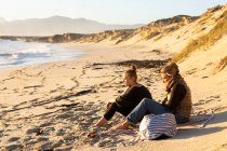 Два человека, мать и дочь, сидят на песке и смотрят в море. — стоковое фото