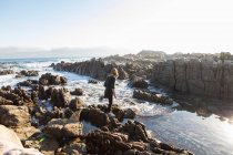 Adolescente marchant à travers des rochers déchiquetés, explorant des piscines rocheuses au bord de l'océan — Photo de stock