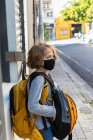 A boy carrying a backpack with a black facemask on a street. — Stock Photo