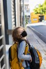 Um menino carregando uma mochila com uma máscara preta em uma rua. — Fotografia de Stock