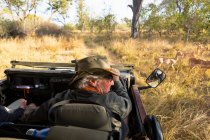 Un guide safari dans un chapeau de brousse au volant d'une jeep regardant un petit groupe d'impala à proximité — Photo de stock