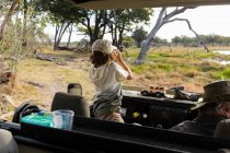 Young boy using binoculars standing up in a safari jeep, looking over the landscape — Stock Photo