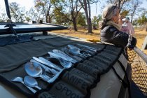 Une pause repas en safari, des boissons, et un rouleau de couverts étalés sur le tableau de bord d'un véhicule safari — Photo de stock