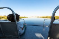 Un garçon sur un bateau à moteur qui longe une voie navigable dans le delta de l'Okavango — Photo de stock