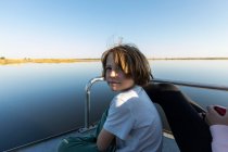 Un garçon sur un bateau à moteur qui longe une voie navigable dans le delta de l'Okavango — Photo de stock