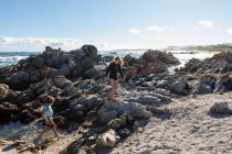 Dos niños, una adolescente y un niño de ocho años explorando las rocas dentadas y las piscinas de rocas en una playa. - foto de stock