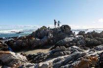 Dos niños, una adolescente y un niño de ocho años explorando las rocas dentadas y las piscinas de rocas en una playa. - foto de stock