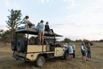 Groupe de personnes debout autour de véhicules safari sur un lecteur de jeu tôt le matin — Photo de stock