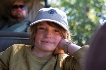 Un chico sentado en un jeep apoyado en su codo en un jeep de safari. - foto de stock