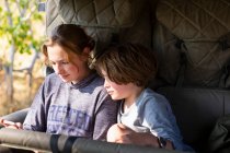 Adolescente et un garçon assis dans une jeep regardant un téléphone intelligent. — Photo de stock