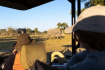 Passagiere im Safari-Jeep beobachten einen großen Elefanten, der in der Nähe des Fahrzeugs läuft. — Stockfoto