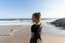 Adolescente debout regardant sur une plage, un garçon courant sur le sable ci-dessous — Photo de stock